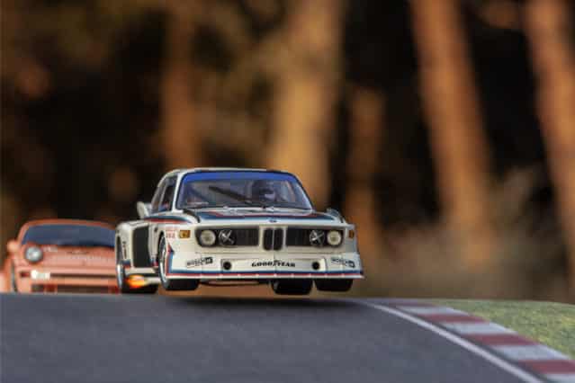 Un BMW 3.0 csl saltando en un cambio de rasante, perseguido por un Porsche 911