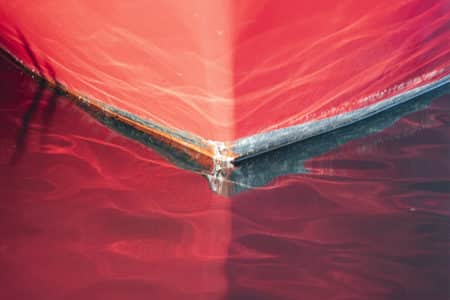 Detalle de la proa de un barco de color rojo que se refleja en el mar.
